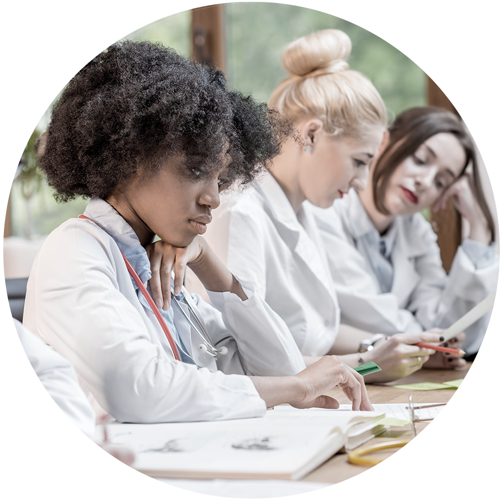 Three women in whitecoats at a desk and taking notes,