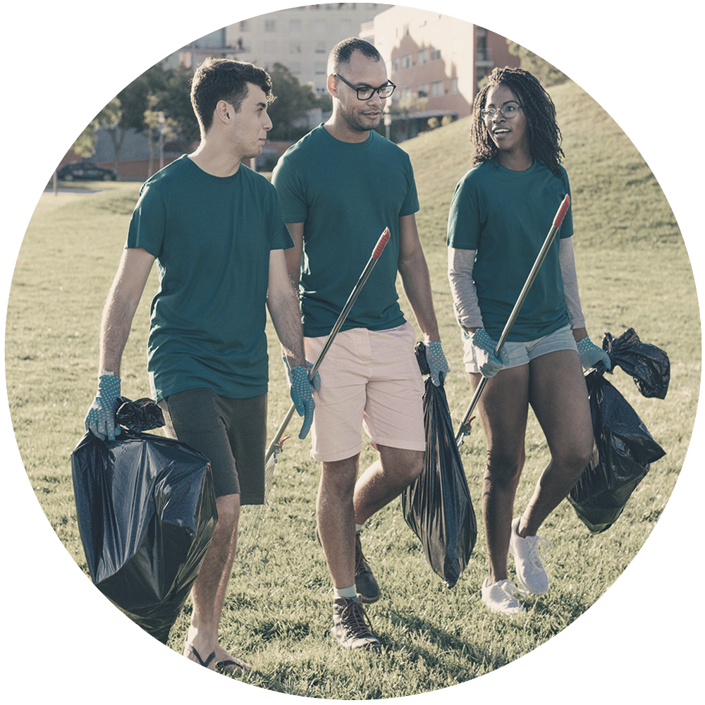 Three people in casual wear in a park holding trashbags and trash pick up sticks