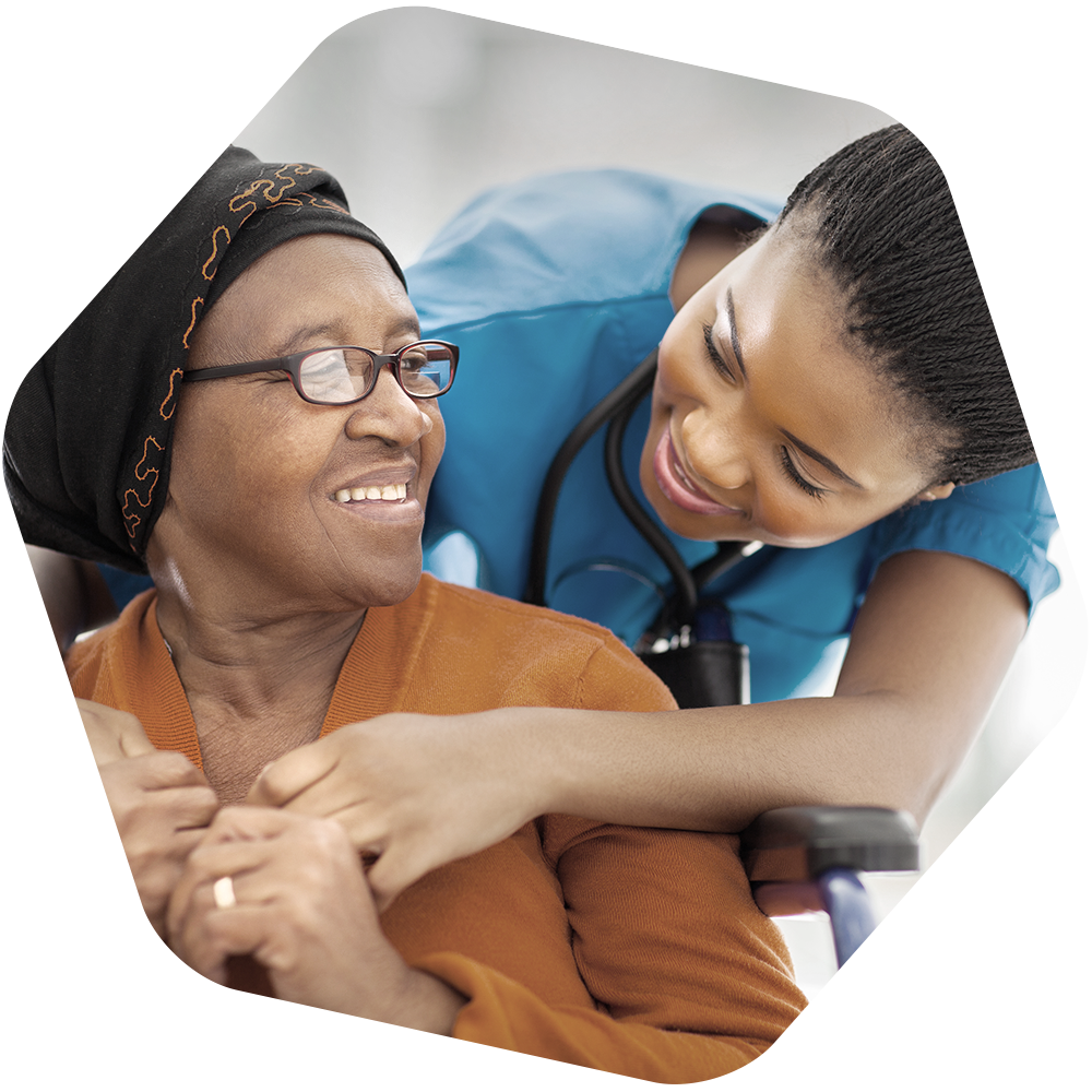 Nurse leans over older woman sitting in a chair in a gesture of care.