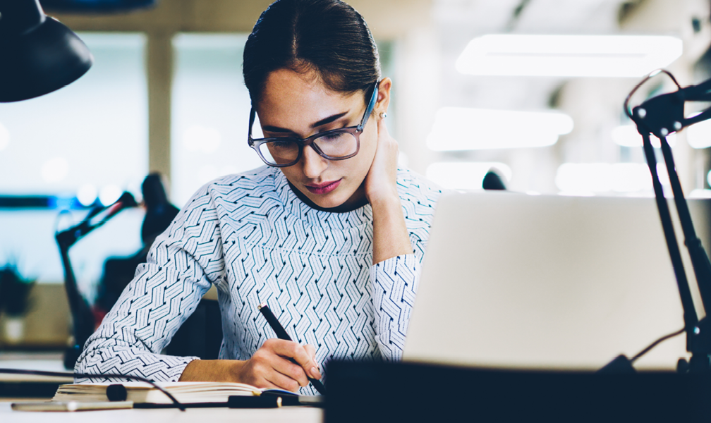 woman sitting at desk writing in front of laptop