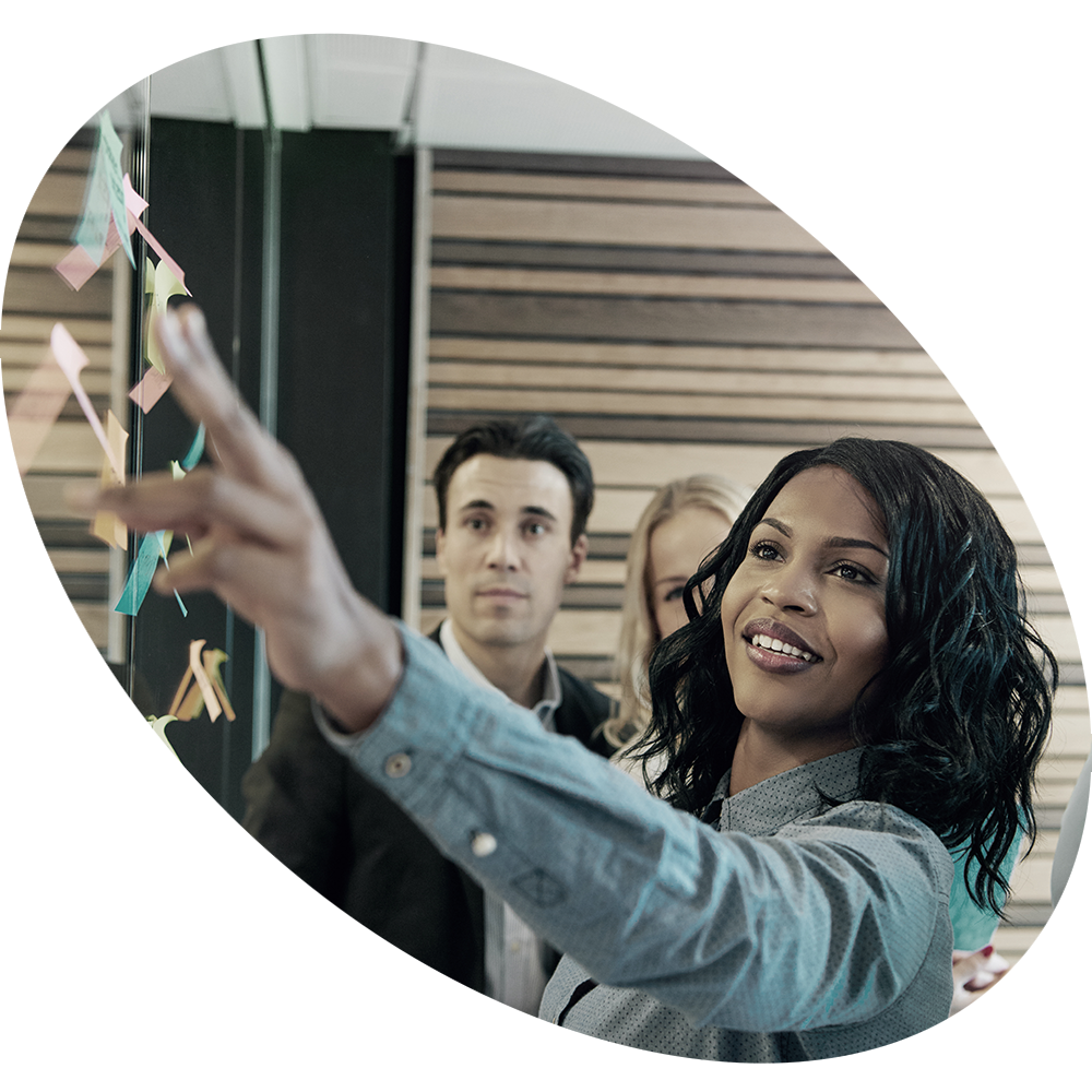 Woman pointing to sticky notes on a wall with colleagues looking over her shoulder