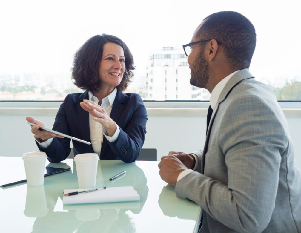 Joyful business woman holding tablet and talking to male colleague in a meeting.
