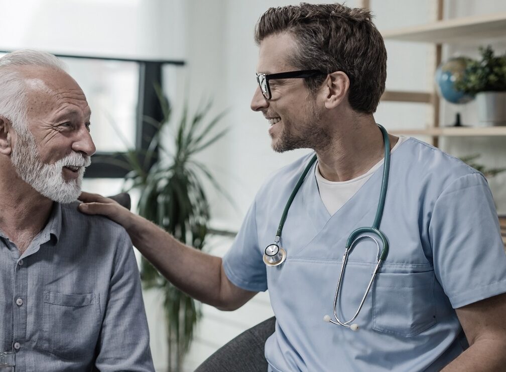 Happy doctor talking to senior male patient while being in a home visit.