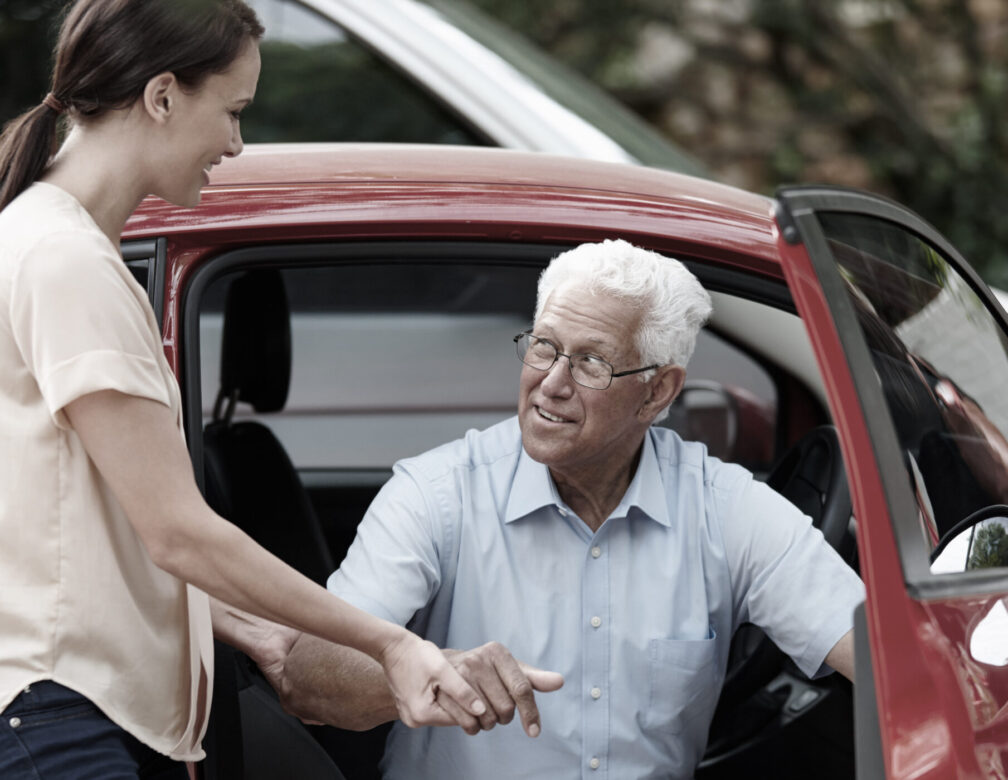 Woman helping older male out of the car.